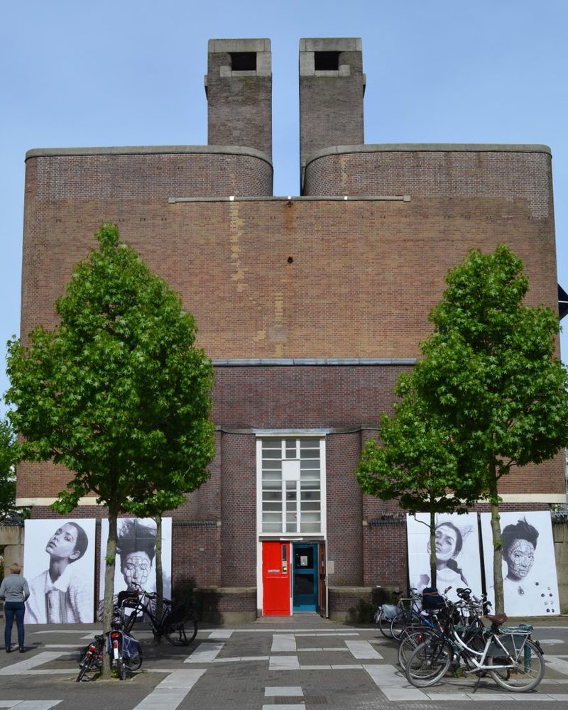 Het kantoor van Koningsgracht Makelaardij aan de Cabralstraat in Amsterdam Oud-West: een bakstenen gebouw in Amsterdamse Schoolstijl met rode voordeur