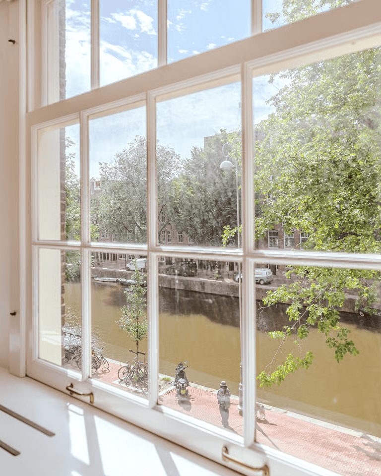 Uitzicht vanuit een Amsterdams appartement op een gracht met bomen