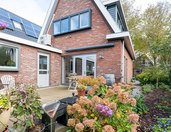 Achtertuin van moderne bakstenen woning met terras, bloeiende planten en zonnepanelen op het dak