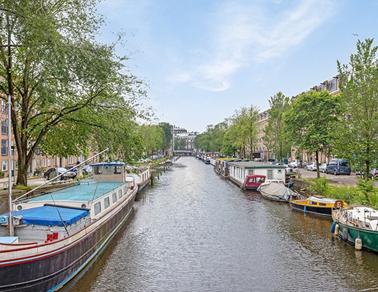 Woonboten en appartementen langs een groene Amsterdamse gracht met uitzicht over het water