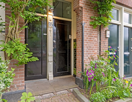 Karakteristieke entree van een bovenwoning in Amsterdam met bakstenen gevel en groene beplanting