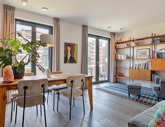 Lichte woonkamer met eethoek, grote raampartijen en toegang tot balkon